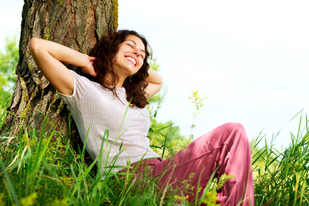 Woman relaxes against a tree and smiles. 